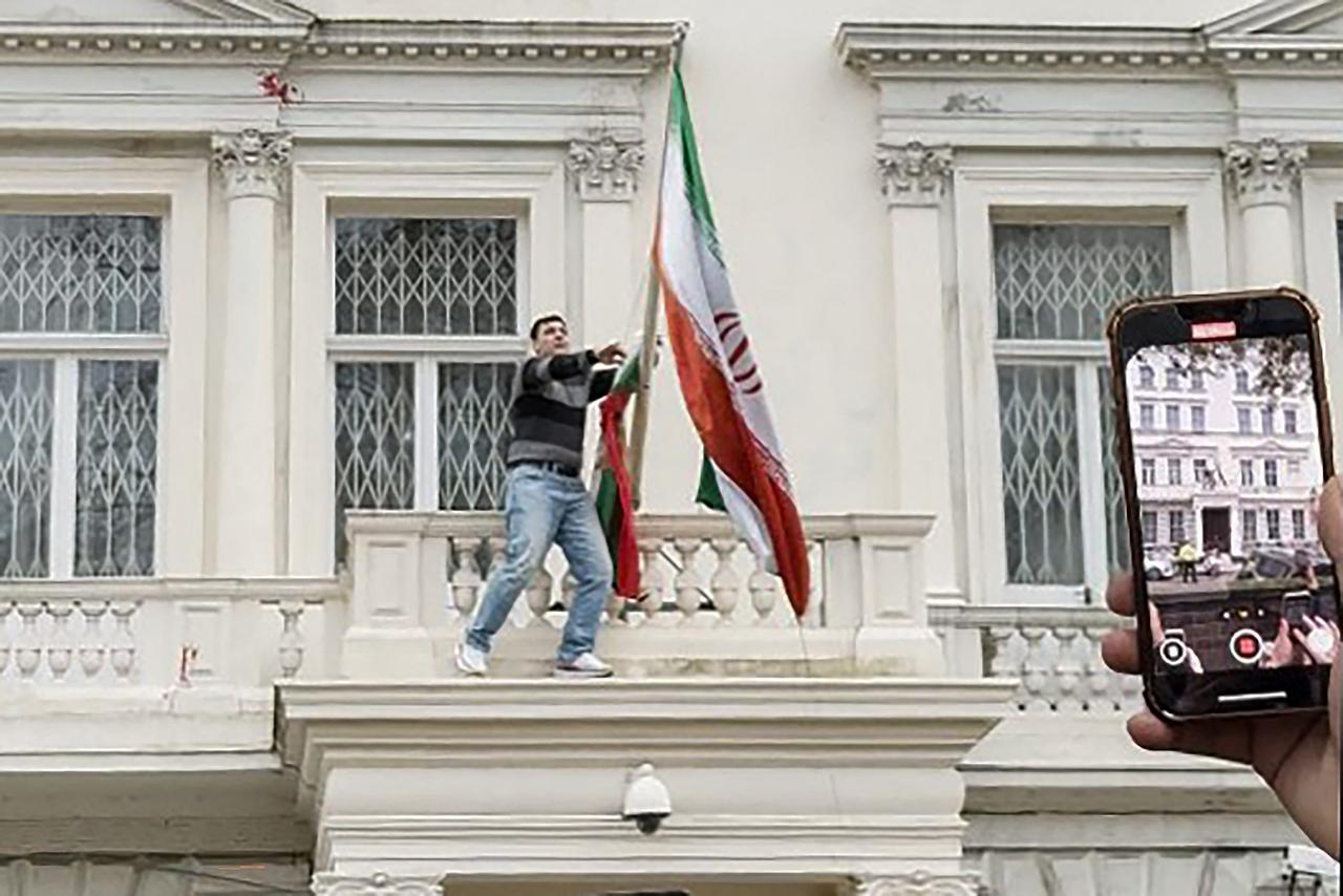 This screen grab taken from a video on January 10, 2026 shows a protester pulling down the Iranian flag from the balcony of Iran's embassy in central London. (AFP Photo / Anonymous UGC via AFPTV)