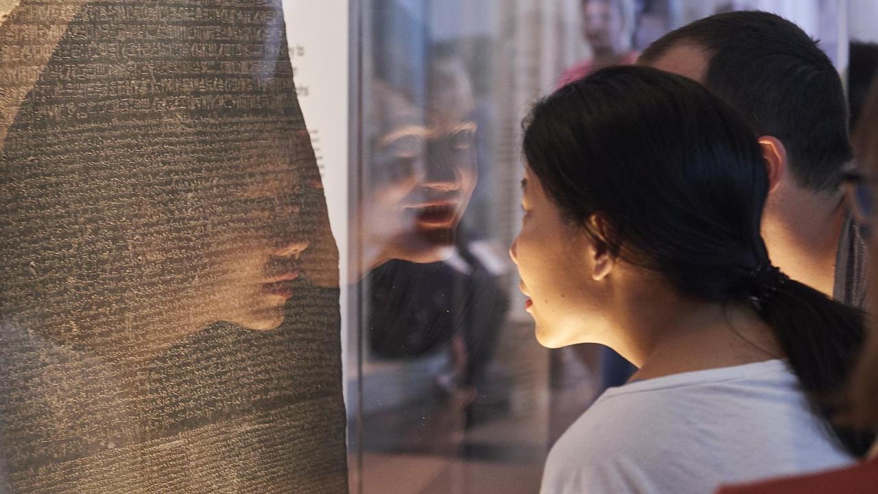 Visitors examine the Rosetta Stone at the British Museum in London instead of Egypt. (Photo via the British Museum)
