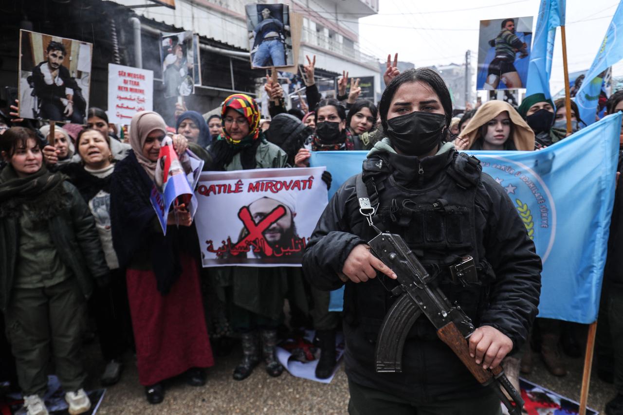 A member of Kurdish security forces stands guard as Syrian Kurds hold a portrait of Syrian President Ahmed al-Sharaa which reads "Killers of Humanity" during a protest in Qamishli, Syria on Jan. 13, 2026. (AFP Photo)