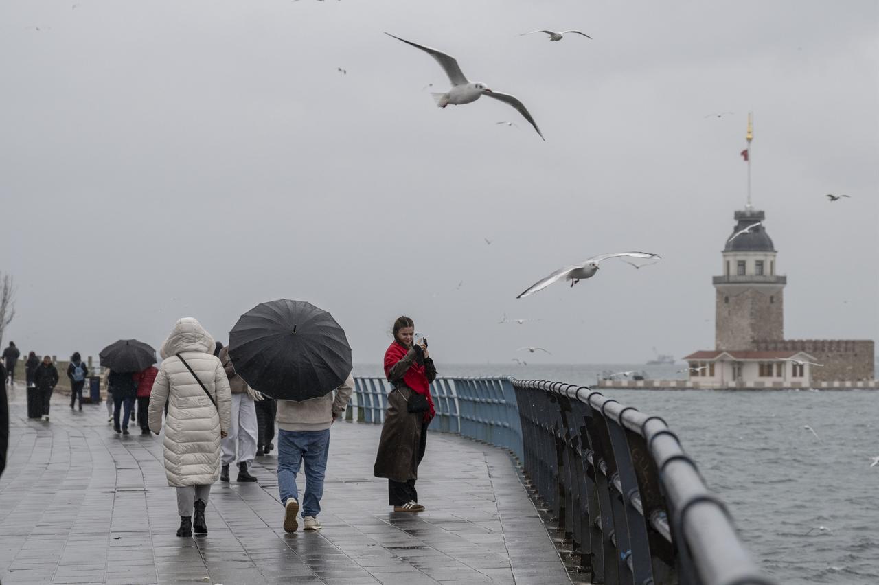 People walk along the seaside near the Maiden’s Tower with umbrellas during heavy rain affected Uskudar Beach, Istanbul, Türkiye, January 11, 2026. (AA Photo)