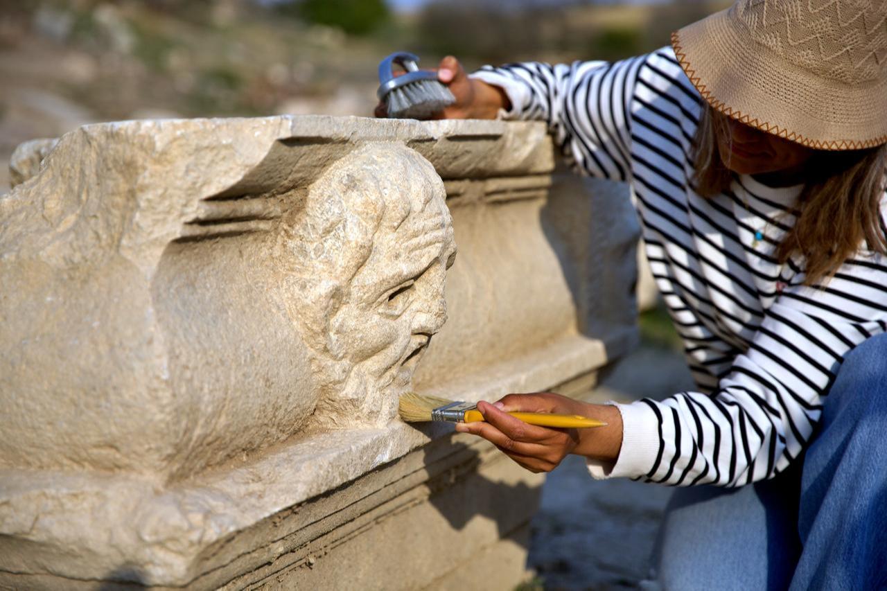 A member of the excavation team cleans the surface of a theatrical mask relief discovered at Kastabala’s Roman theater, Osmaniye, southern Türkiye, Nov. 19, 2025. (AA Photo)
