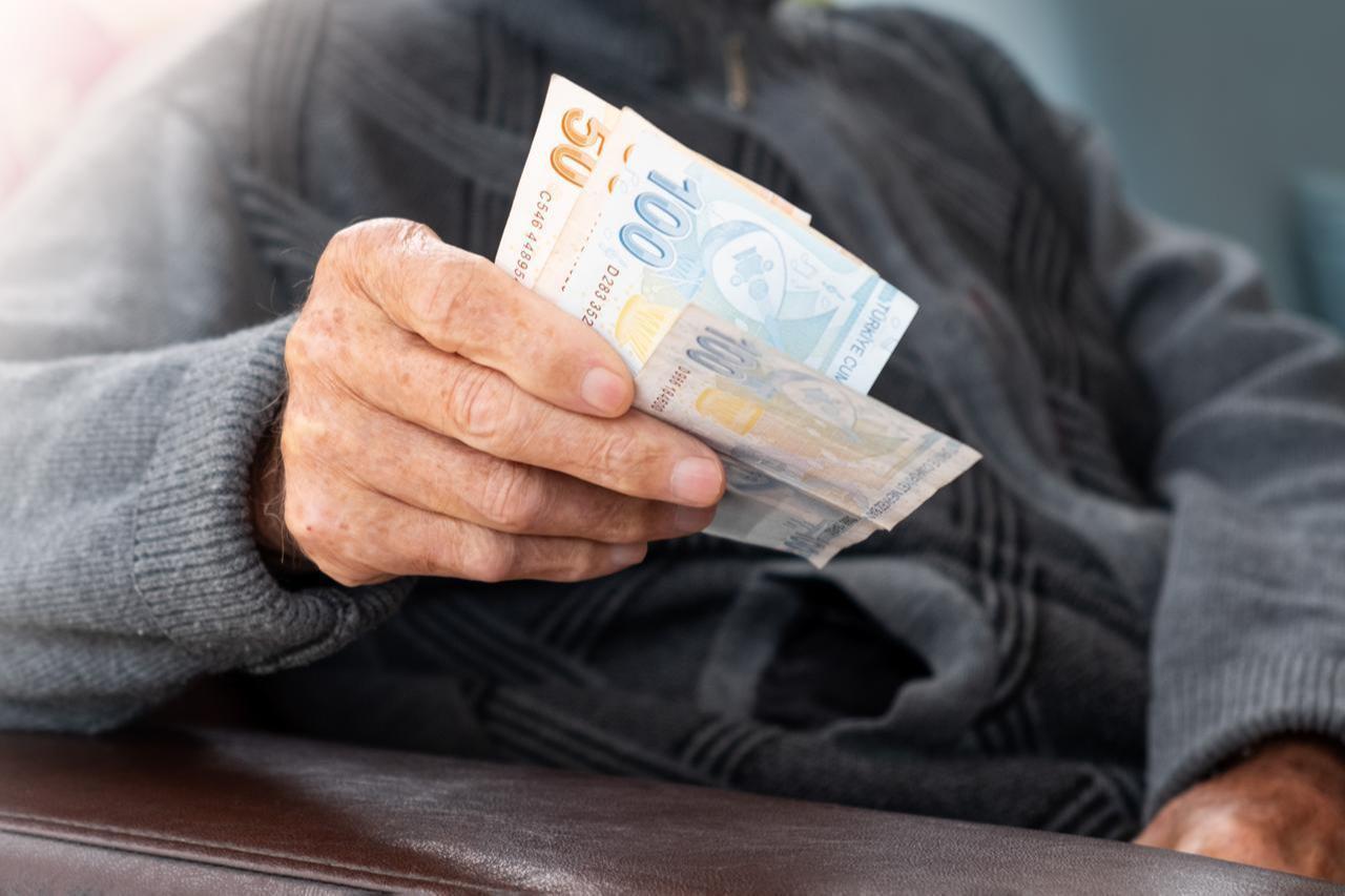 Elderly person holds Turkish lira banknotes at home in Türkiye. (Adobe Stock Photo)