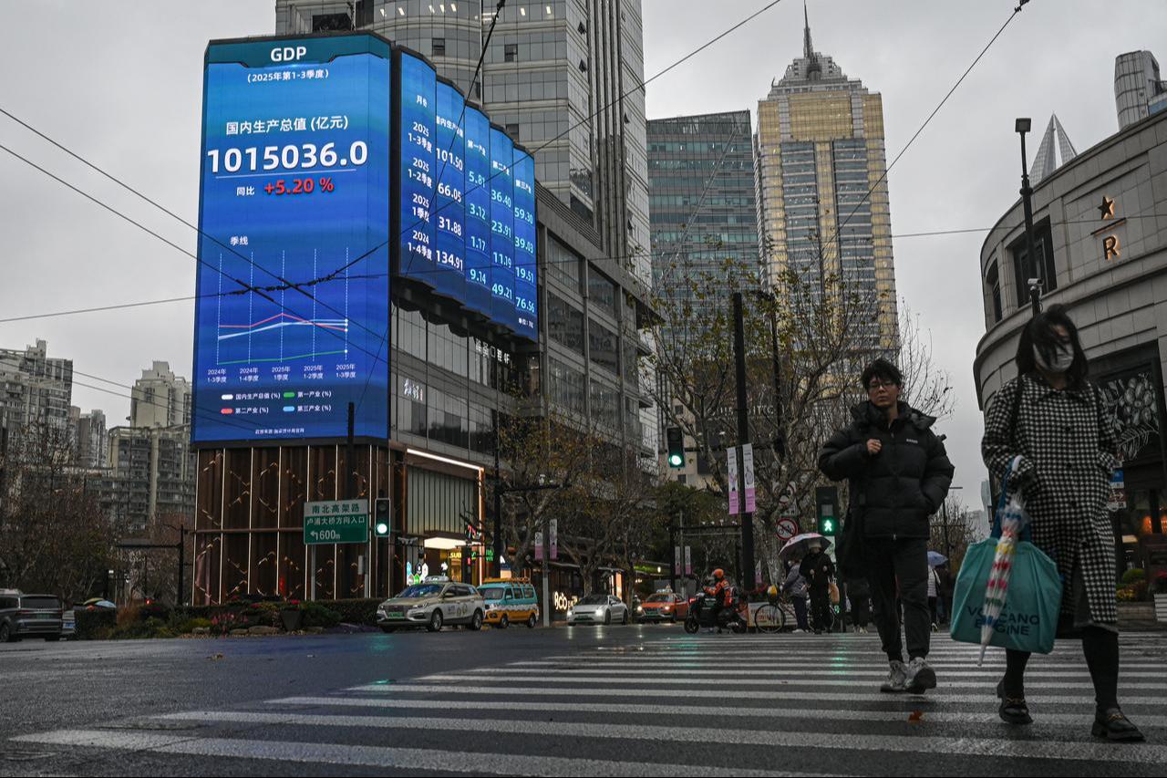 People walk past a screen showing figures of the gross domestic product (GDP) on a street in Shanghai, January 19, 2026. (AFP Photo)