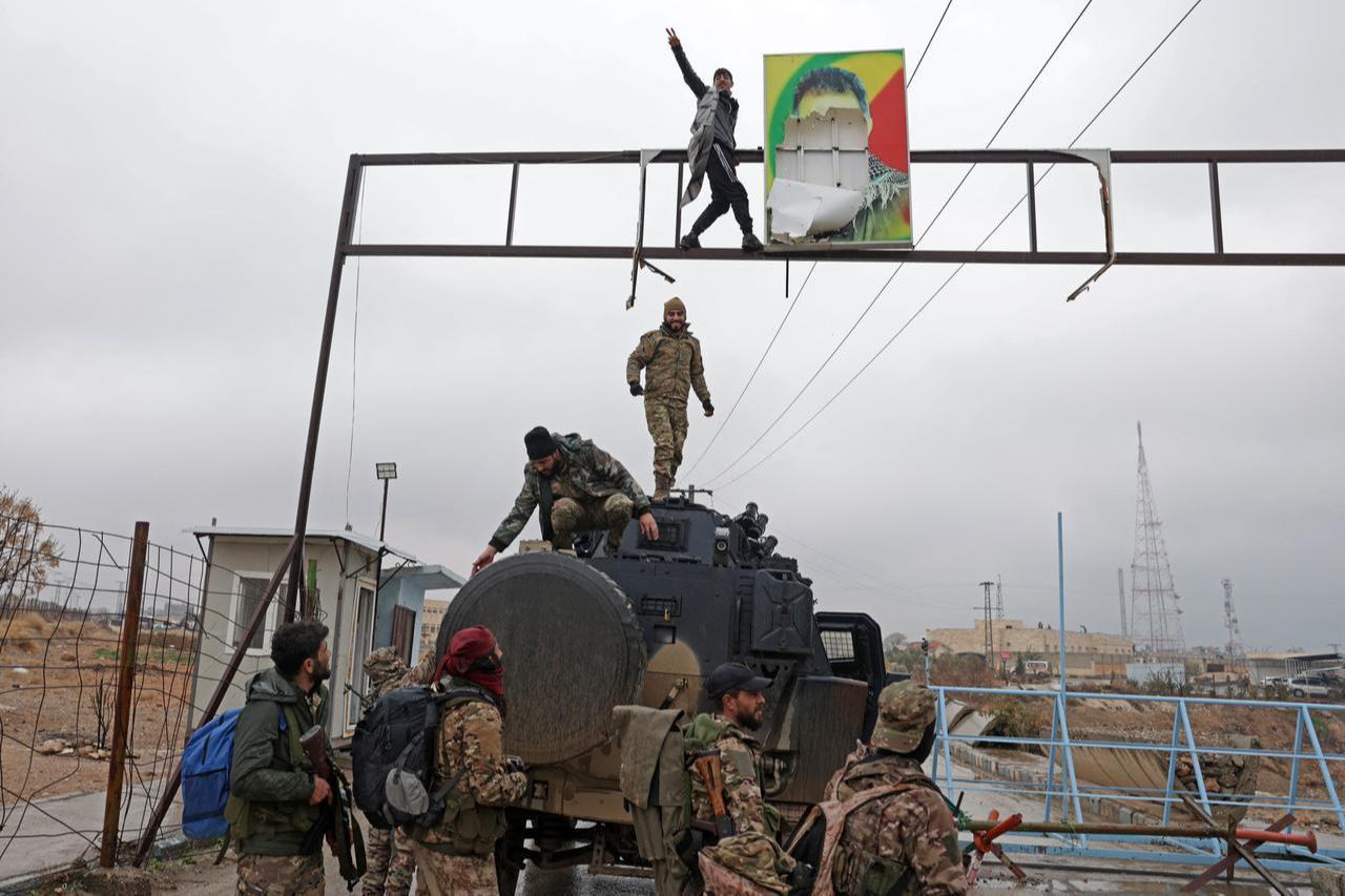 A man gestures next to a torn portrait of jailed PKK ringleader Abdullah Ocalan installed along a street as Syrian army personnel watch in Tabqa, in Raqqa province, Syria, Jan. 18, 2026. (AFP Photo)