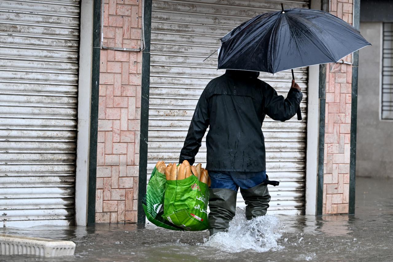 A man carries a bag of bread as he wades through floodwaters in La Goulette, near the capital Tunis, on January 20, 2026. ( AFP Photo )