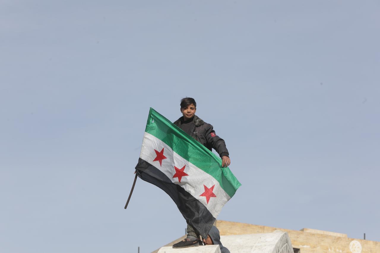 A young person holds a Syrian flag as Syrian families wait for their loved ones around al-Aktan prison, near Raqqa on January 21, 2026. (AA Photo)