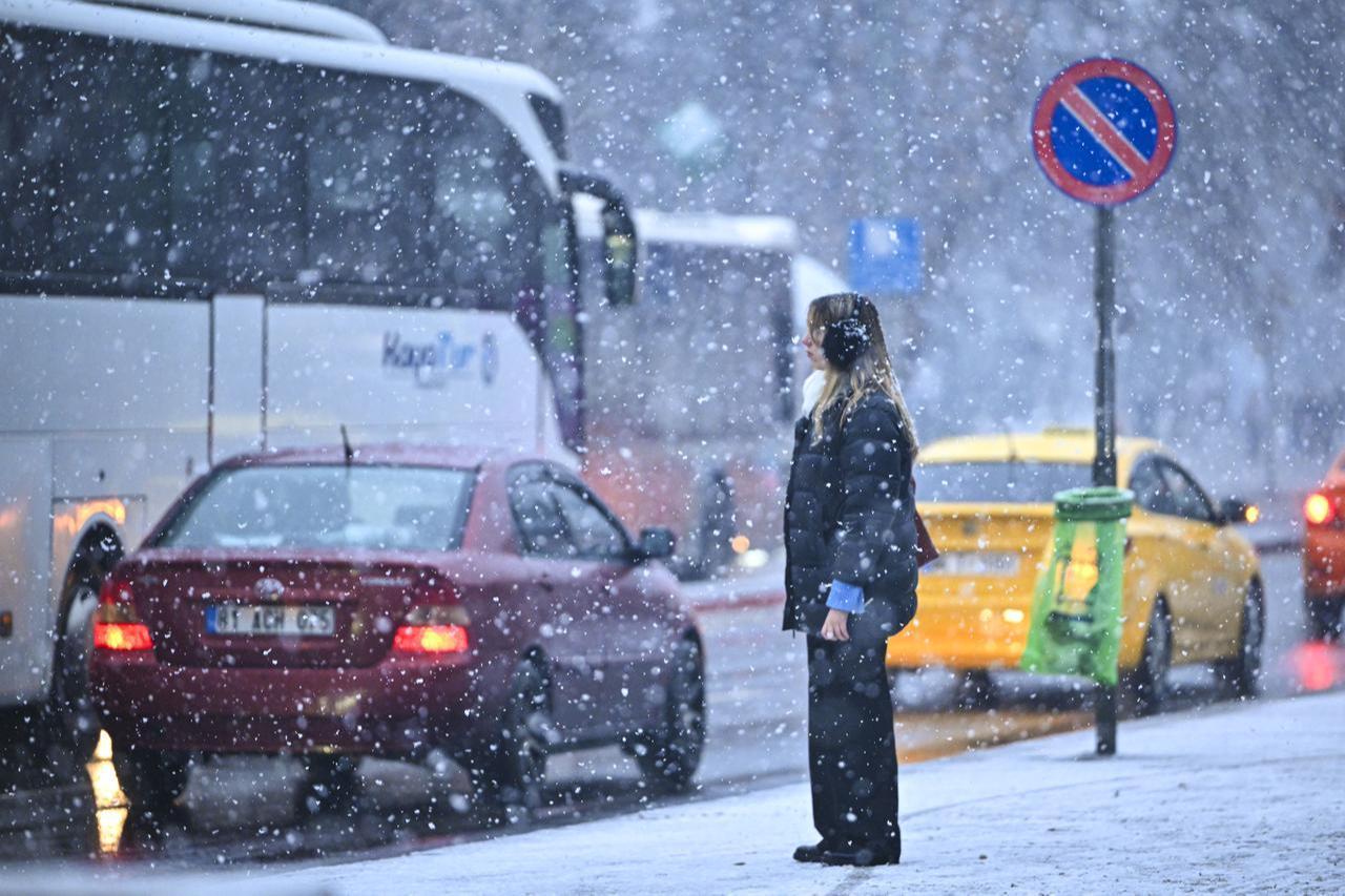 A woman waits to get cross during snowfall in the evening hours in Ankara, Türkiye on January 22, 2026. (AA Photo)