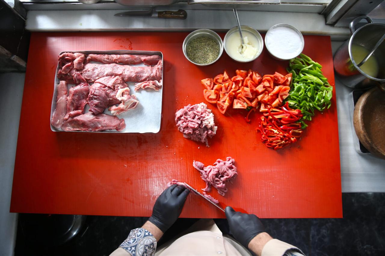 A cook carefully chops the lamb before arranging it with the vegetables in the tray. (AA Photo)