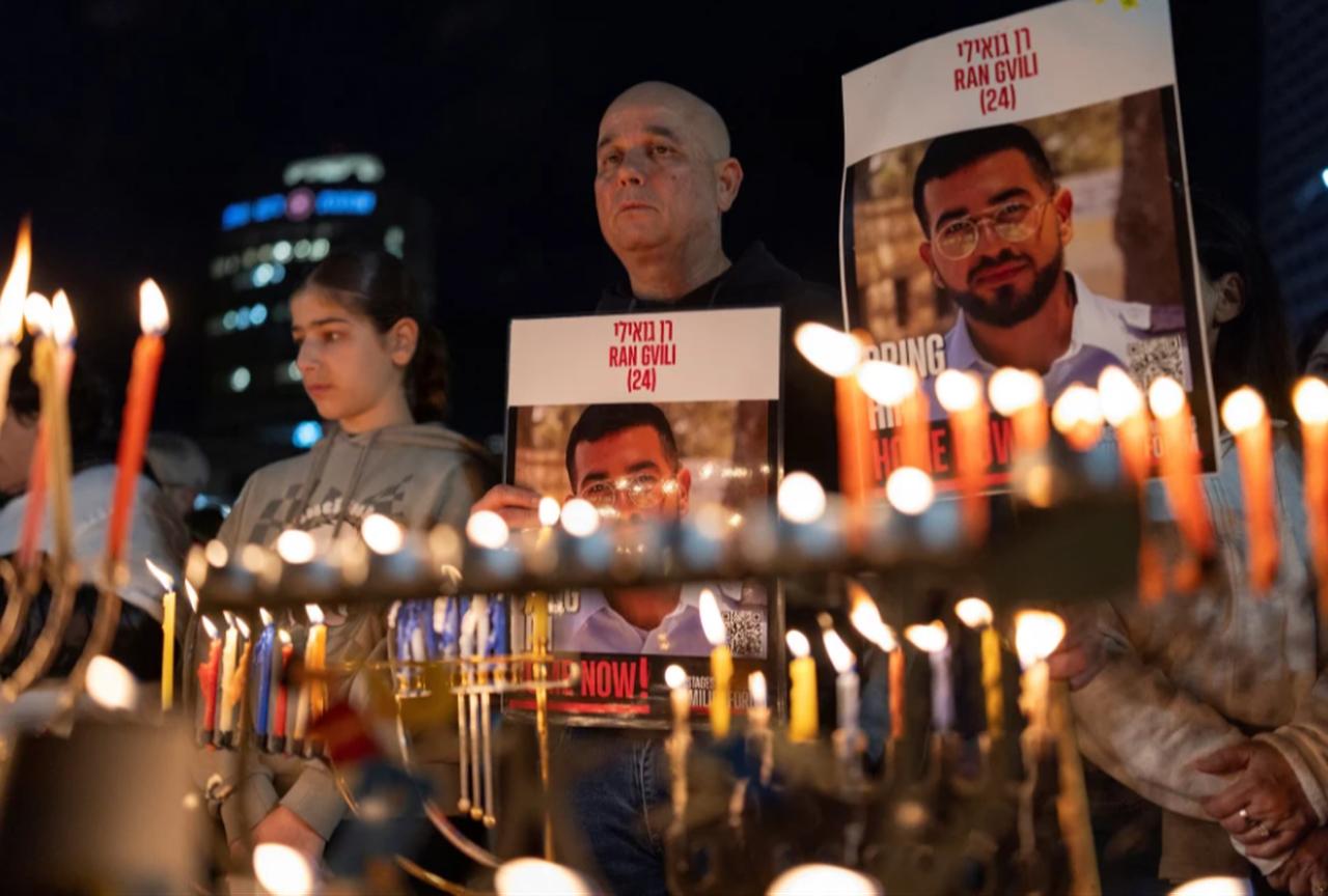 Israelis light the eighth candle of Hanukkah in Hostage Square holding placards bearing the face of Ran Gvili in Tel Aviv on Dec. 21, 2025.  ( AFP Photo)