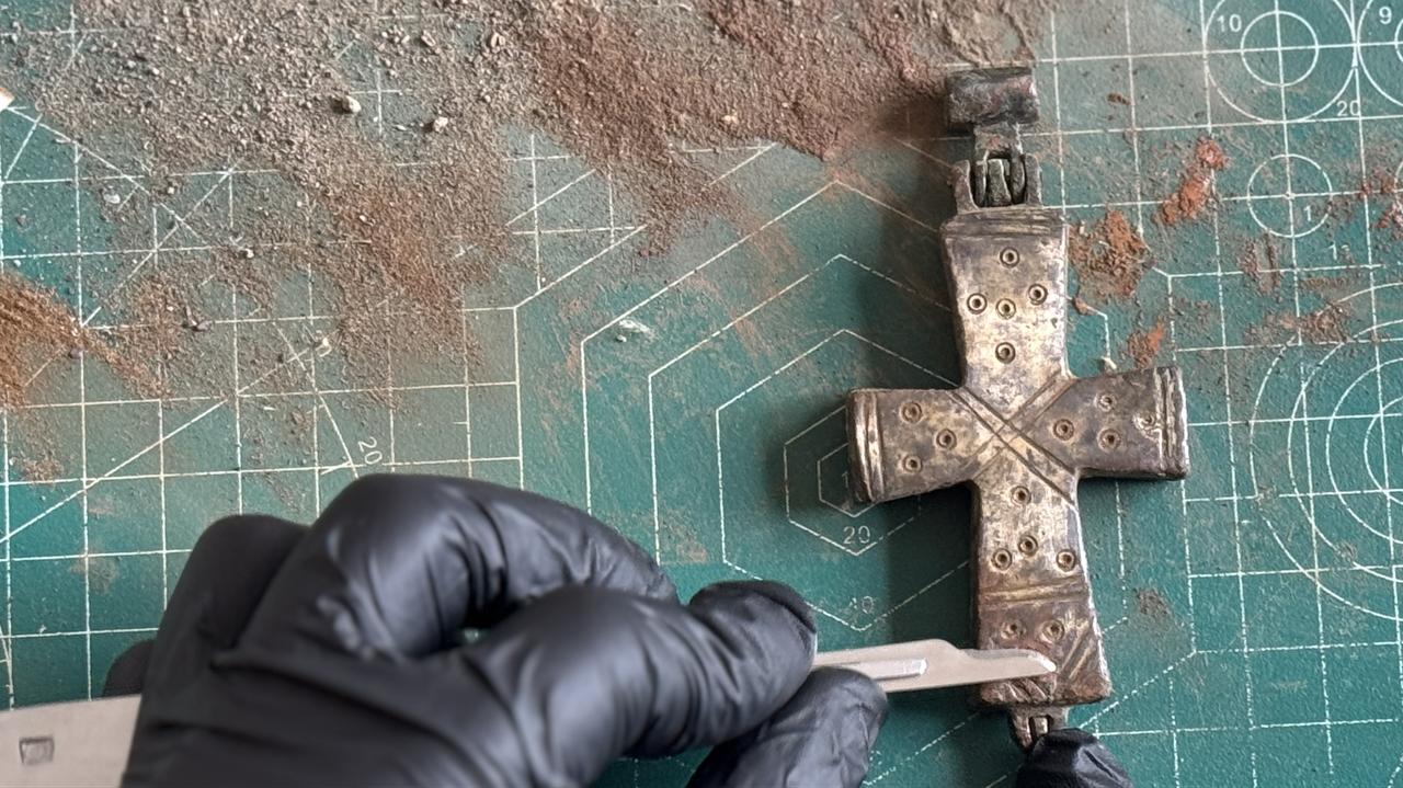 A conservator carefully cleans corrosion from a sealed medieval bronze reliquary cross discovered during excavations at the ancient city of Lystra in Konya, central Türkiye, Jan. 27, 2026. (AA Photo)
