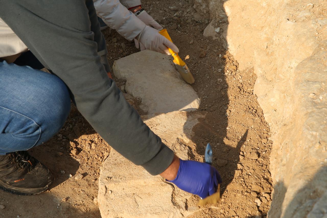 An archaeologist carefully brushes soil from a stone structure resembling a T-shaped pillar during rescue excavations near the Ataturk Dam reservoir in the Samsat district of Adiyaman, southeastern Türkiye, Jan. 27, 2026. (AA Photo)