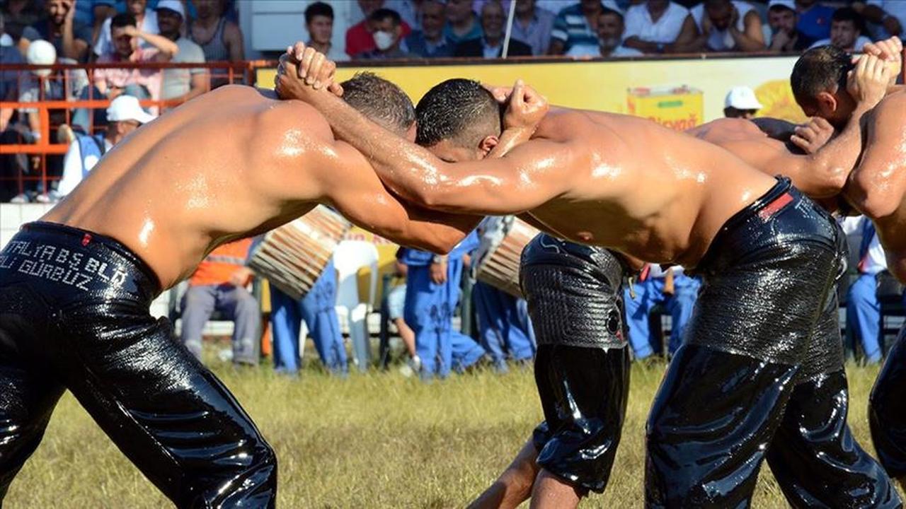 Two wrestlers, slick with oil and clad in traditional kispet, grapple intensely in the center of the field during the third‑round başpehlivanlık matches at the historic Kırkpınar Oil Wrestling Festival. (Anadolu Agency via aa.com.tr)