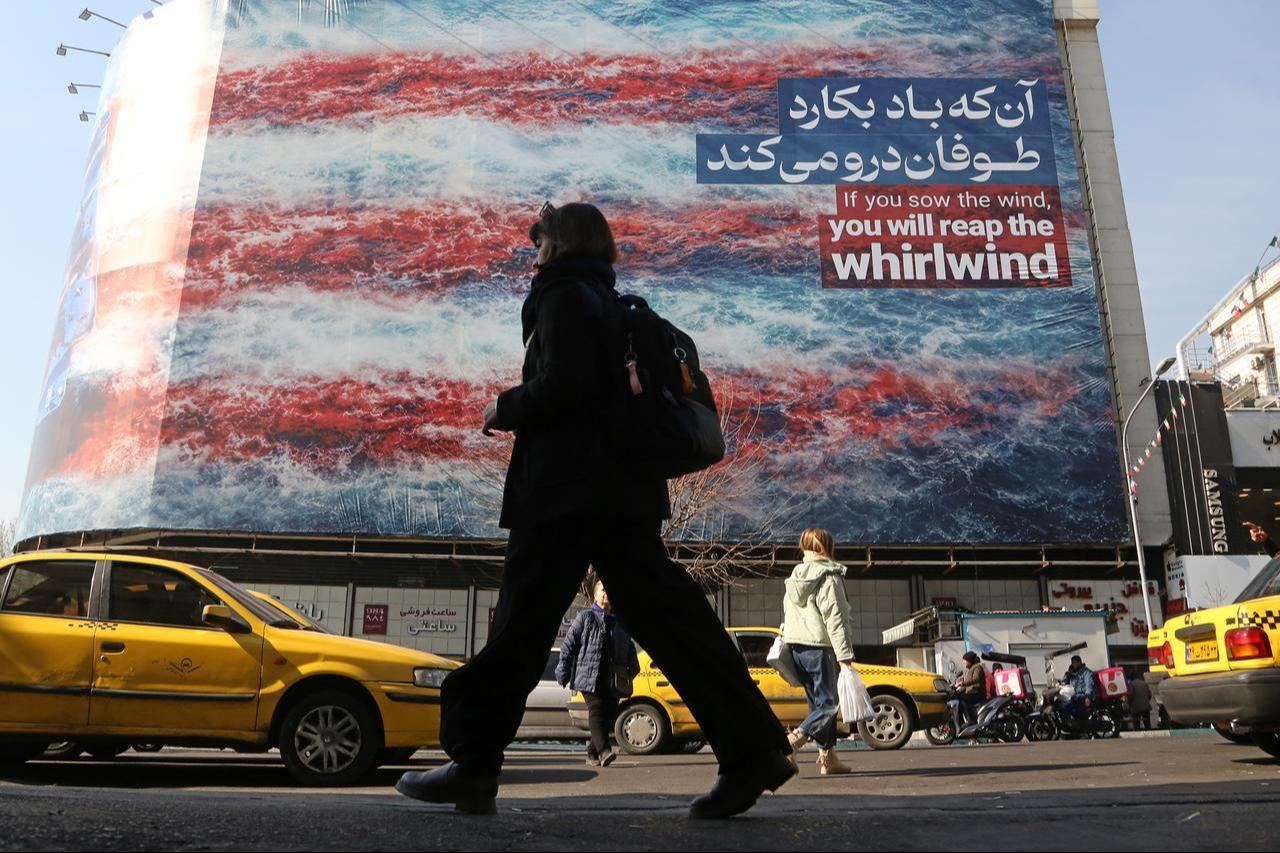 People walk past an anti-American wall poster that reads "If you sow the wind, you will reap the whirlwind." following a possible US intervention, in Tehran, Iran, January 28, 2026. (AA Photo)