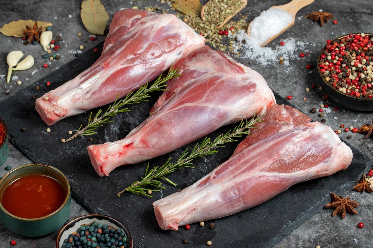 Raw goat leg cuts displayed with herbs and spices before cooking. (Adobe Stock Photo)