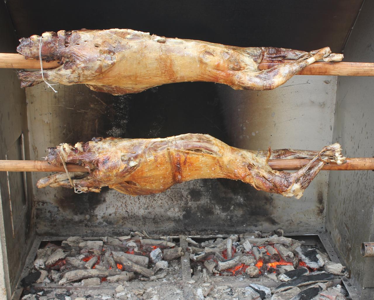 Kid goat roasting on a horizontal spit above a wood fire. (Adobe Stock Photo)