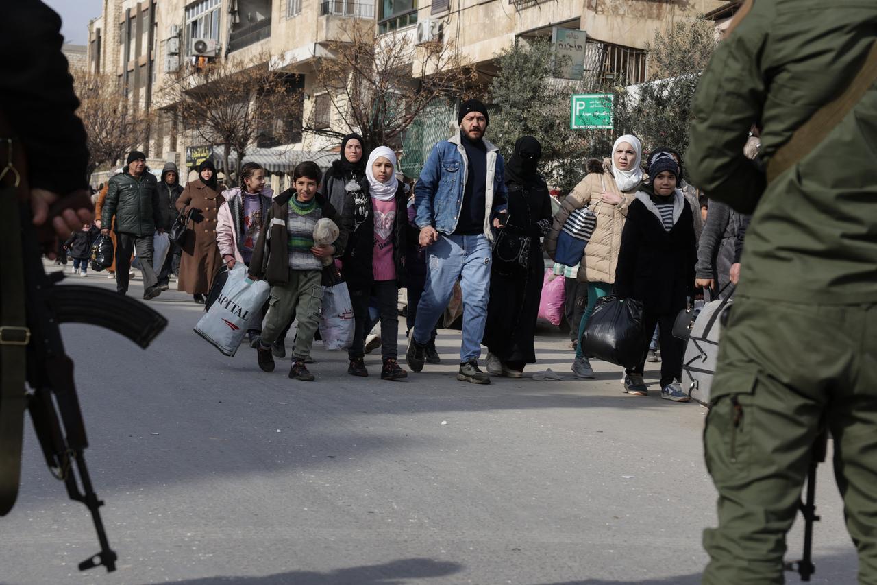 Children carrying belongings walk past security forces as residents flee the Ashrafieh neighbourhood of Aleppo on January 7, 2026. (AFP Photo)