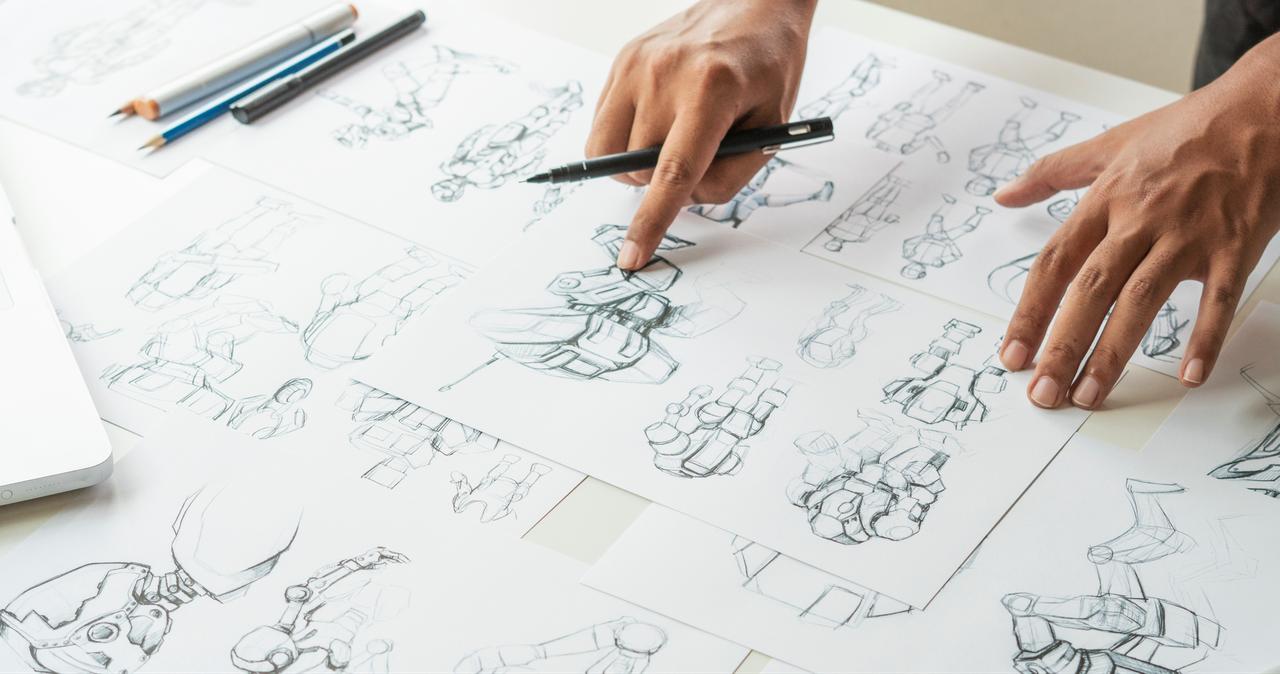 A designer reviews concept sketches and character drawings spread across a worktable. (Adobe Stock Photo)