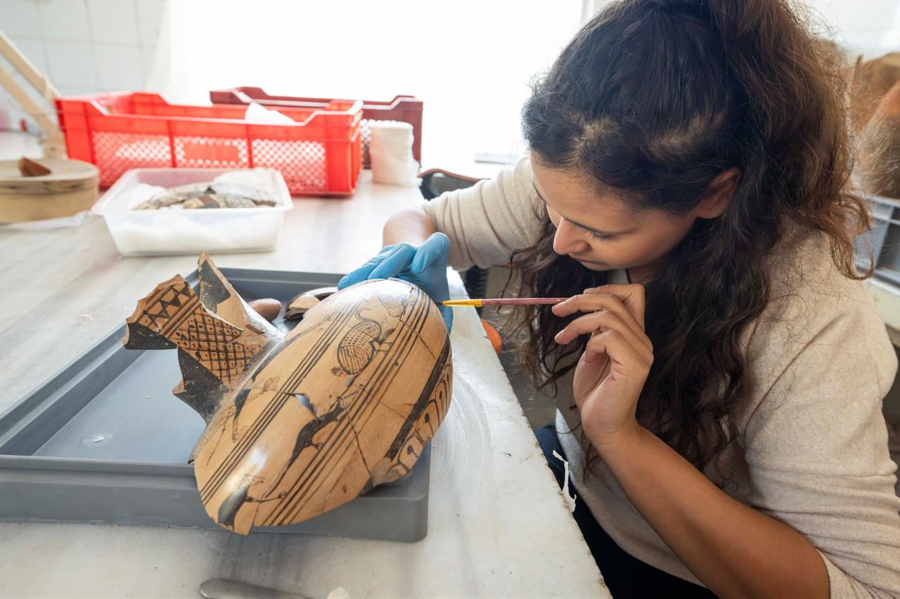 An archaeologist carefully cleans and examines a decorated ceramic vessel recovered during excavations at Smyrna Mound in Izmir, western Türkiye, October 14, 2026. (AA Photo)