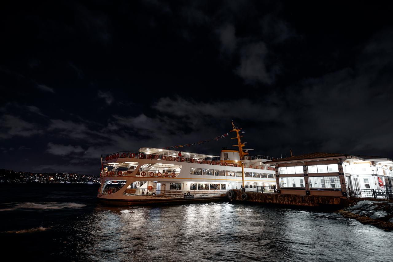 Bright Istanbul ferry moored at a waterfront terminal at night, reflecting across the Bosphorus under a deep blue sky.