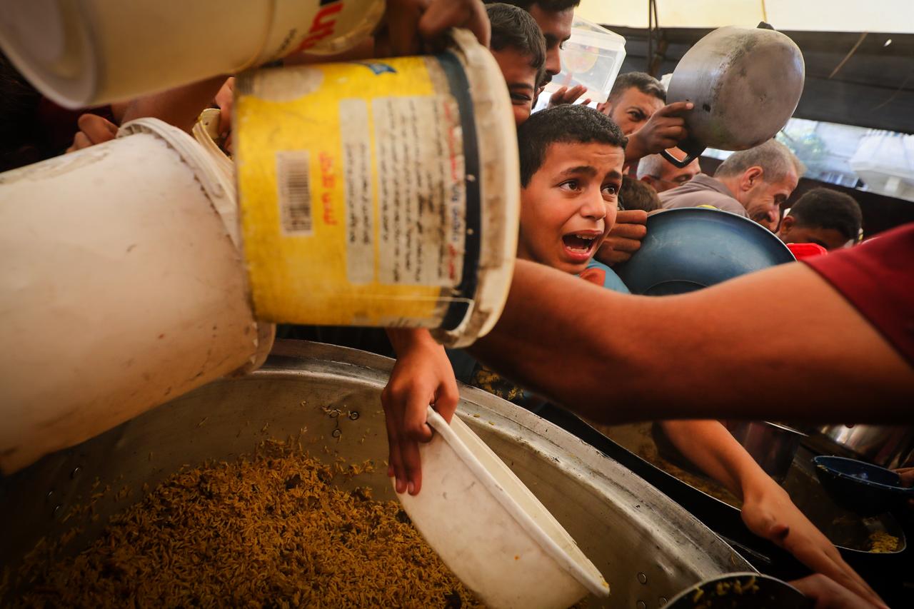 Displaced Palestinians, including numerous children holding empty containers and cooking pots, crowd around a community aid distribution center to receive hot meals in the Nuseirat refugee camp, central Gaza Strip, Palestine on October 17, 2026. (AA Photo)