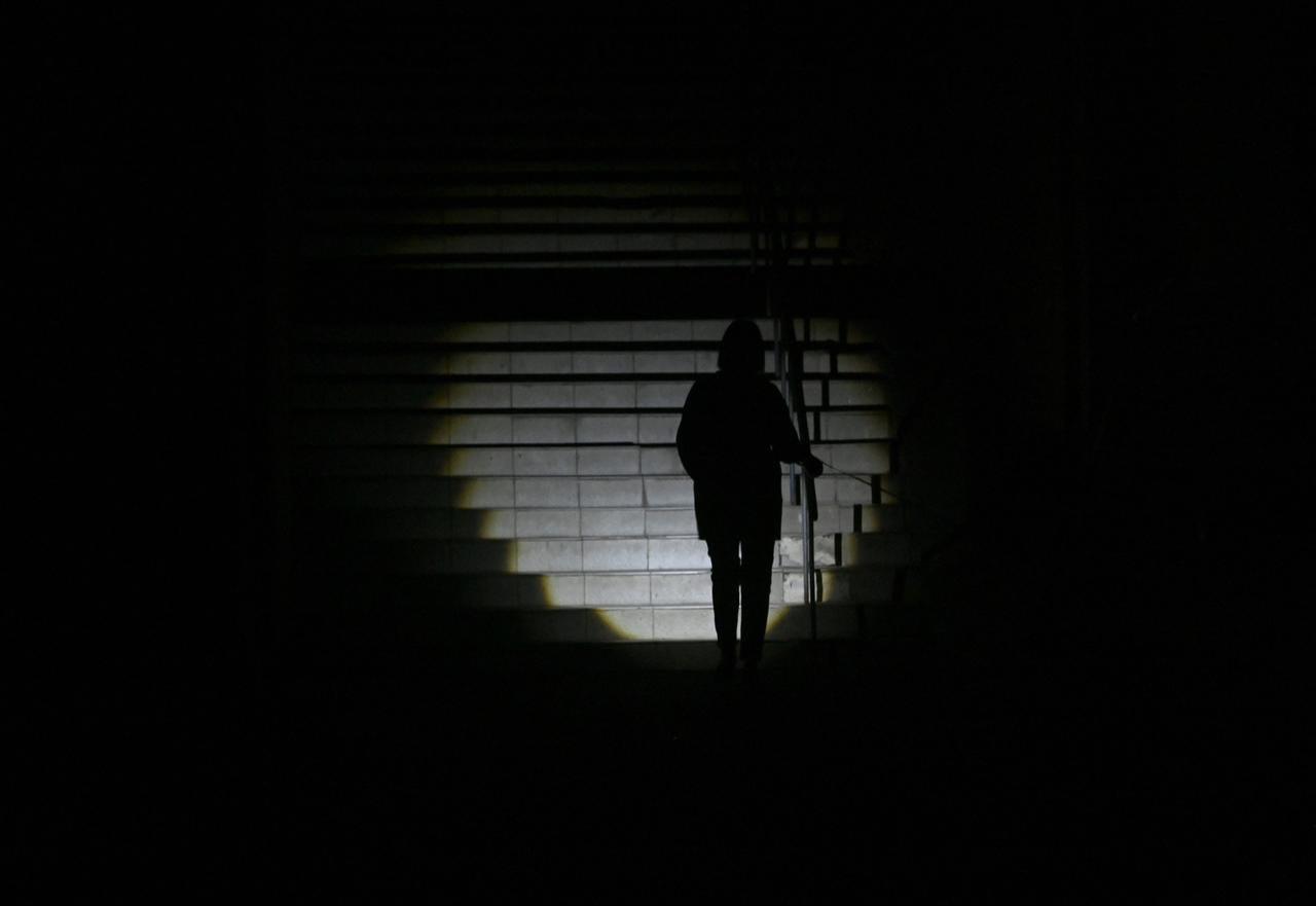 A woman uses a torch as she climbs stairs in a dark street during a blackout in Kyiv on October 8, 2026. (AFP Photo)
