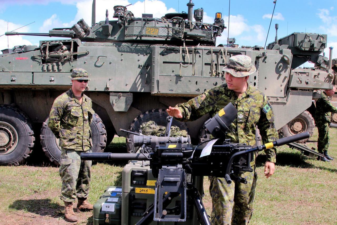 Canadian soldiers demonstrate a mounted weapon system in front of an armored military vehicle during a training exercise. (US Army Photo)