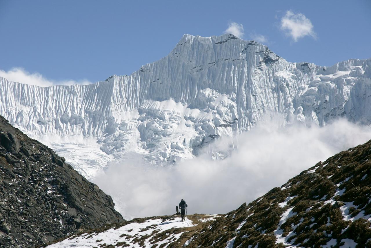 A mountaineer approaches a towering, snow-covered mountain face in the Himalayas. (Adobe Stock Photo)