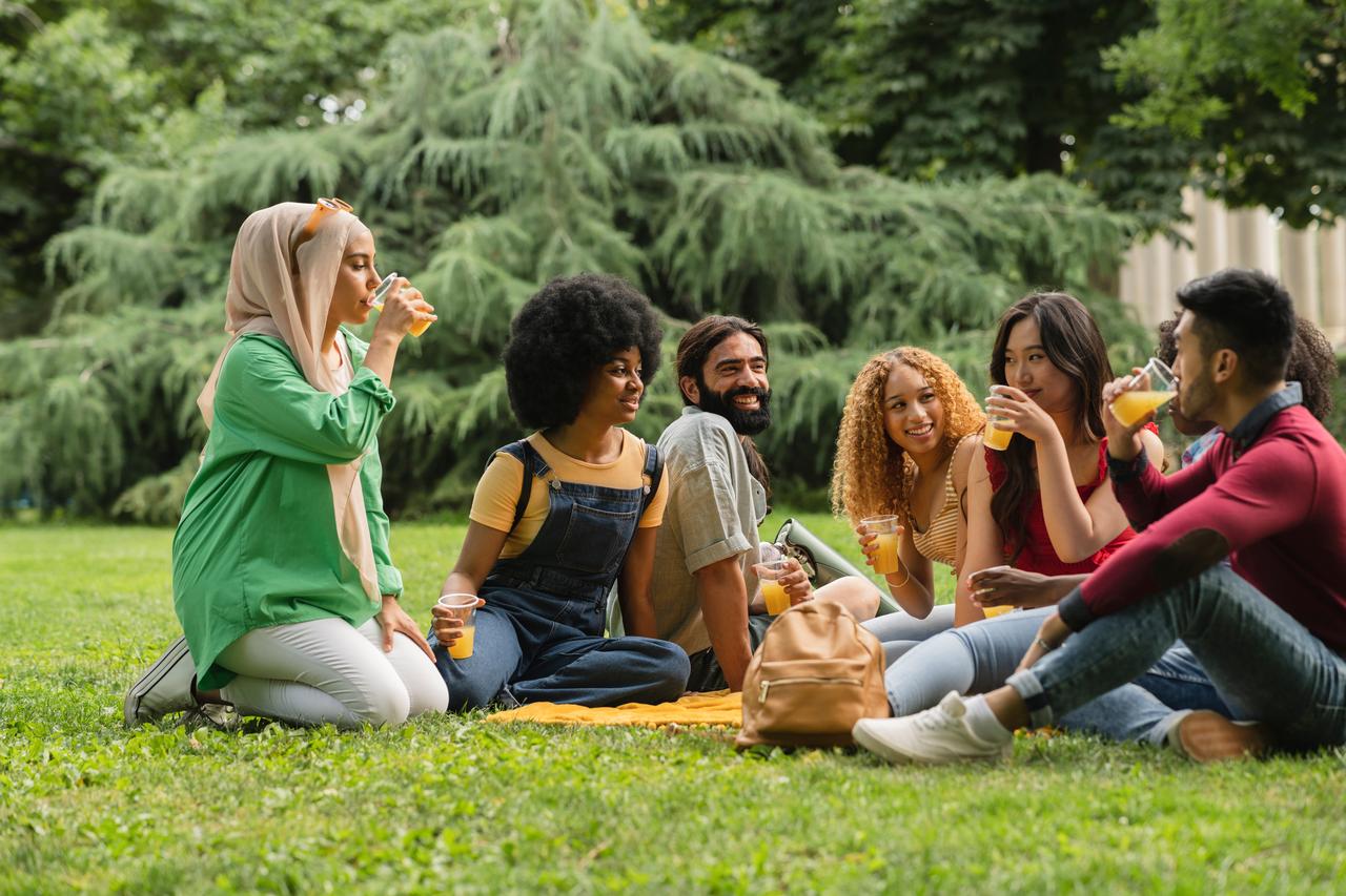 A diverse group of young adults socializes outdoors in a park, undated. (Adobe Stock Photo)