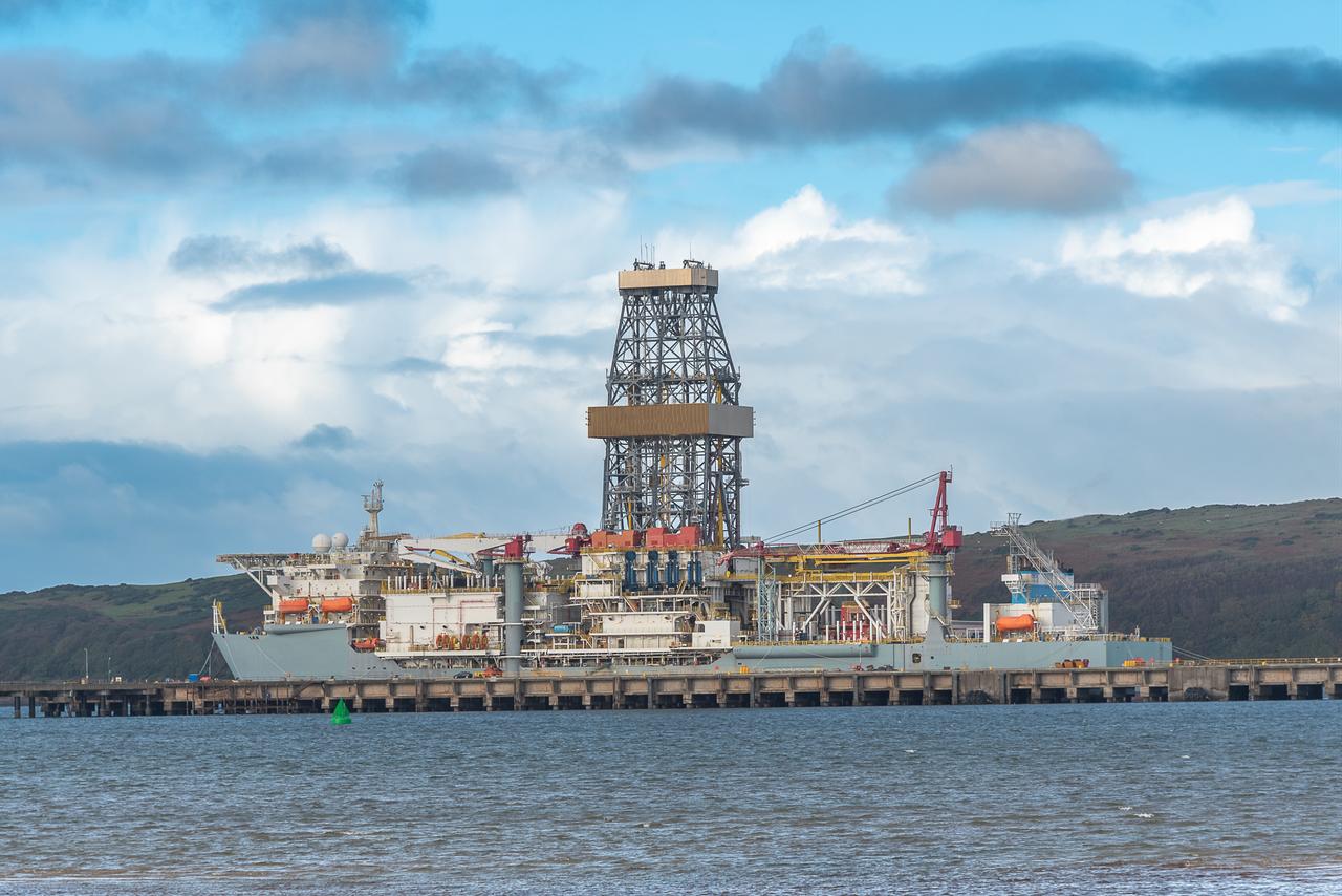 An offshore drilling vessel equipped with a large drilling tower is docked at a port. (Adobe Stock Photo)