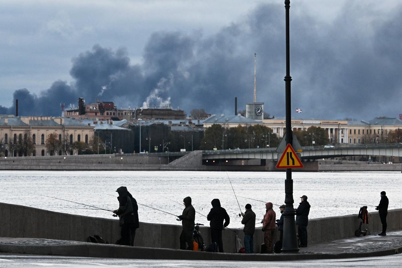 Fishermen fish on the Neva River as smoke rises above the city following an air attack on the oil terminal in Saint Petersburg on October 18, 2026. (AFP Photo)