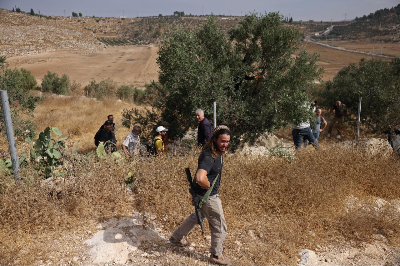 An armed Israeli settler evacuates Palestinians and Israeli activists from the area of olive tree plantation in Idna village near the occupied West Bank town of Hebron, Oct. 13, 2026. (AFP Photo)