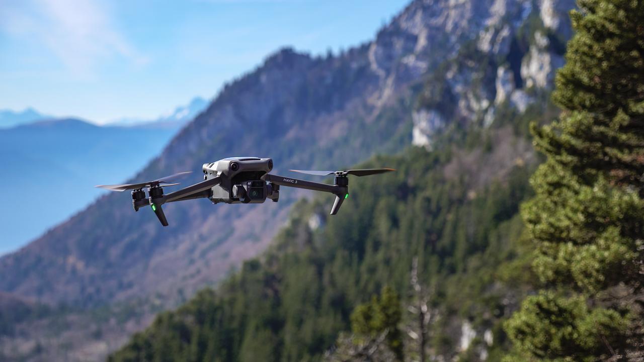 A DJI Mavic 3 drone flies over a mountainous, forested landscape. (Adobe Stock Photo)