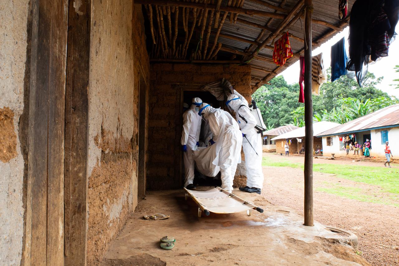Health workers wearing protective suits carry a covered body from a house in a rural African village during an infectious disease response. (Adobe Stock Photo)