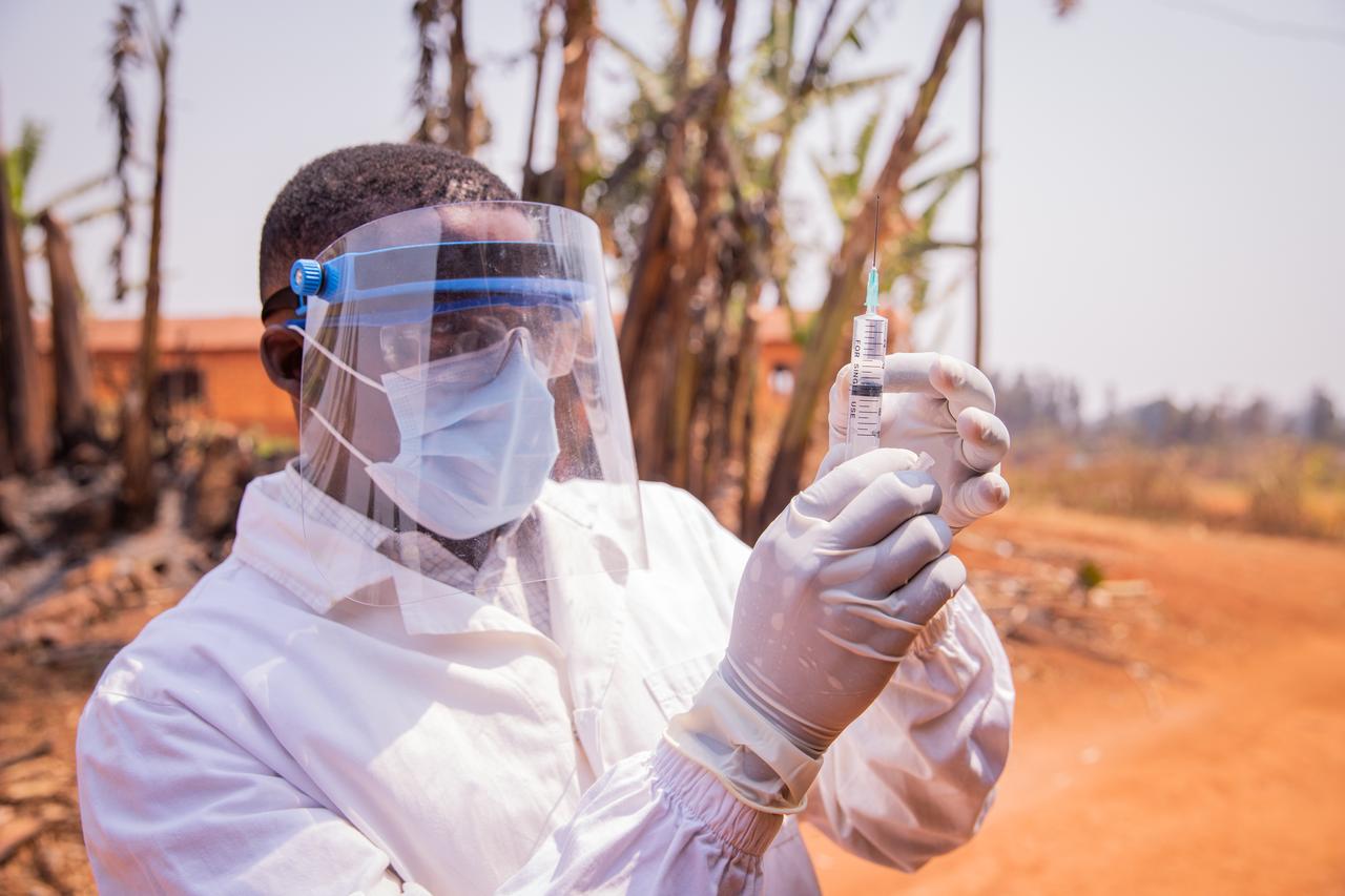 A health worker wearing a face shield, mask and gloves prepares a syringe during a medical procedure outdoors. (Adobe Stock Photo)
