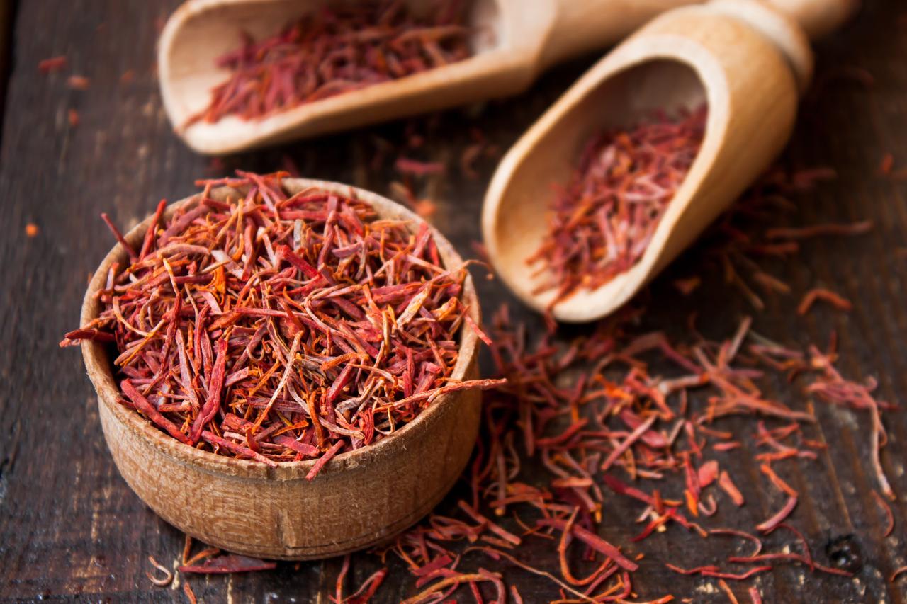 Dried saffron threads are displayed in a wooden bowl and scoops on a rustic wooden surface. (Adobe Stock Photo)