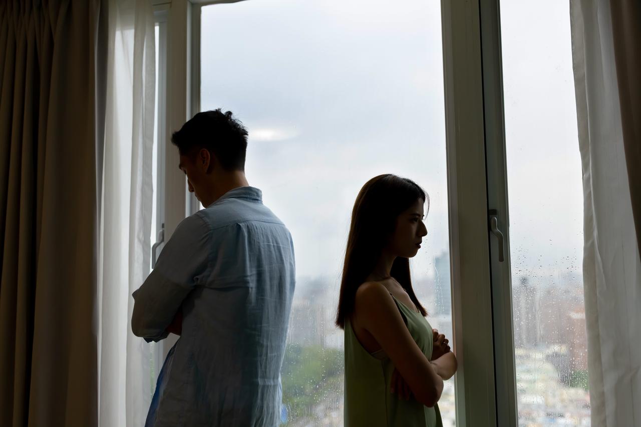 A couple turn away from each other by a window. (Adobe Stock Photo)