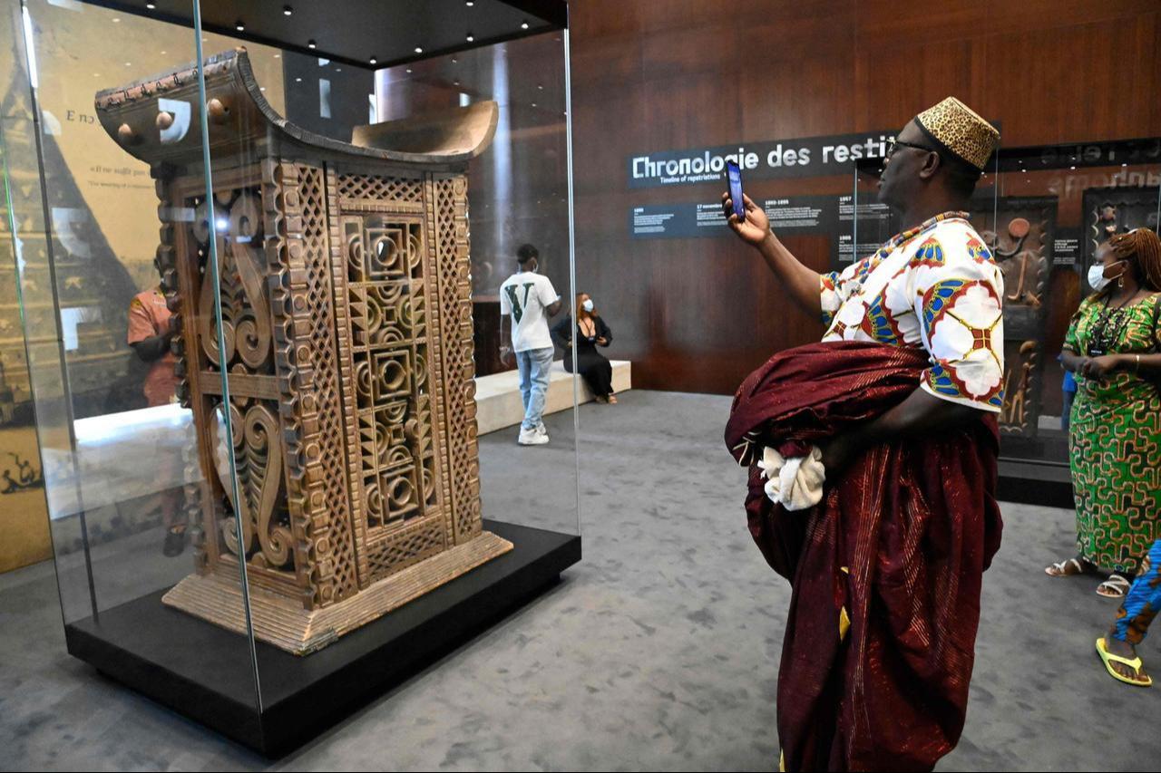 A man in traditional wares photographs with his smartphone the ceremonial throne of King Ghezo, one of the artifacts looted by French colonial soldiers returned and displayed for viewing by the general public during an exhibition at the presidency in the capital Cotonou, Benin, Feb. 20, 2022. (AFP Photo)