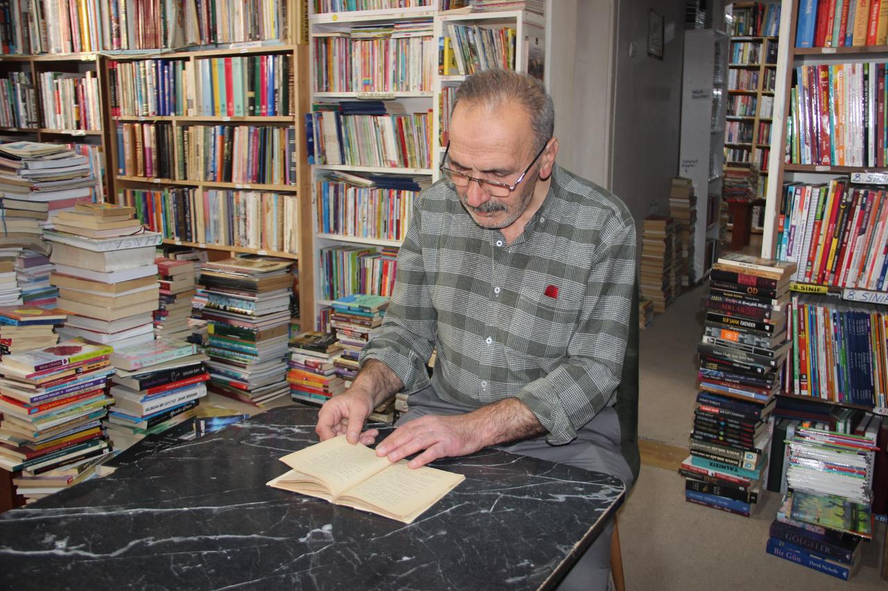 Secondhand bookseller Nizamettin Korucu examines a rare 1928 Ottoman Turkish edition of Russian author Grigory Petrov's The Idealist Teacher at his bookstore in Erzurum, Türkiye, Oct. 21, 2026. (IHA Photo)