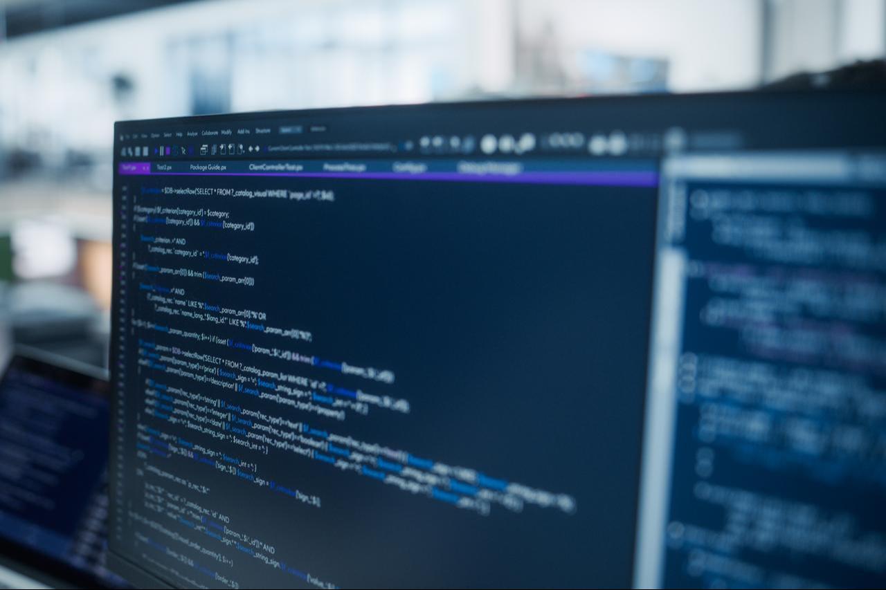Computer monitors display SQL and PHP source code at a software development workstation in an open-plan technology office. (Adobe Stock Photo)
