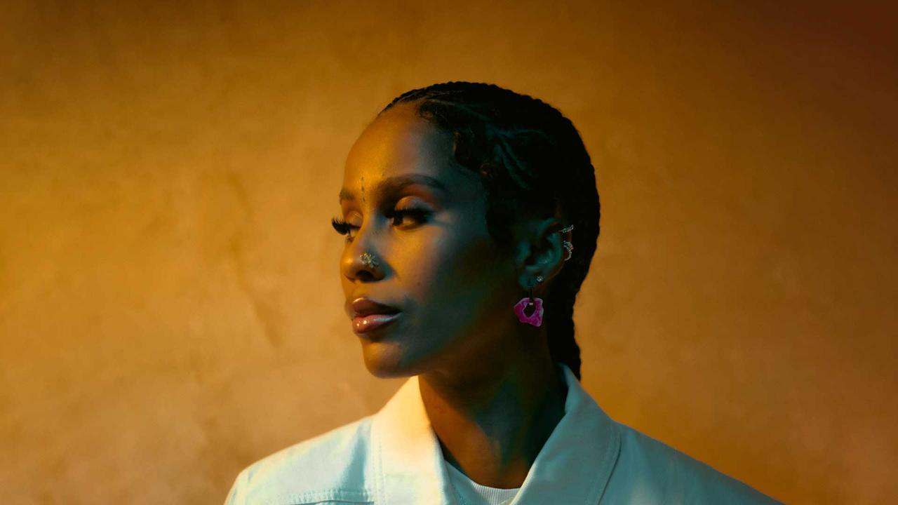 UK-based Angolan-Portuguese rapper IAMDDB poses for a portrait against a warm orange background. (Photo via Live Nation)