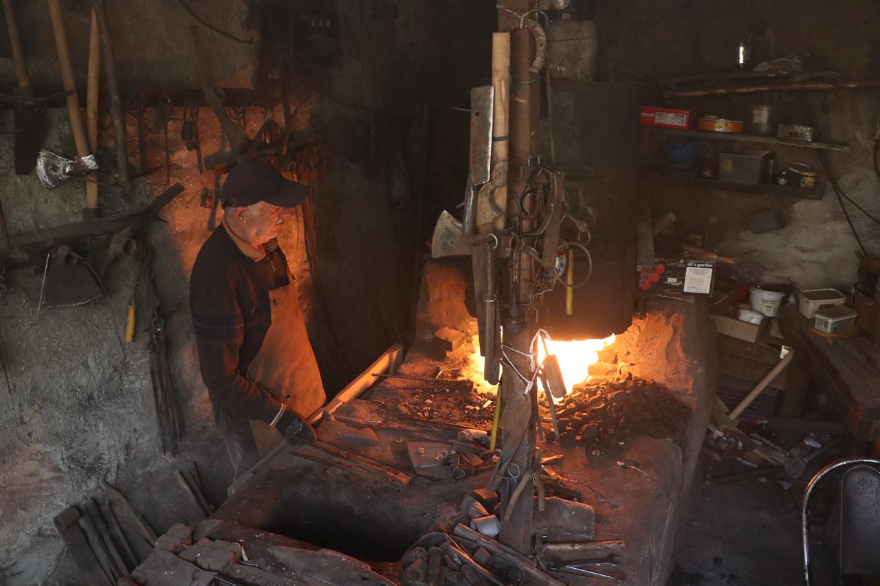 Blacksmith Remzi stands beside a burning forge surrounded by traditional ironworking tools in his workshop in Türkiye, Oct. 23, 2026. (AA Photo)