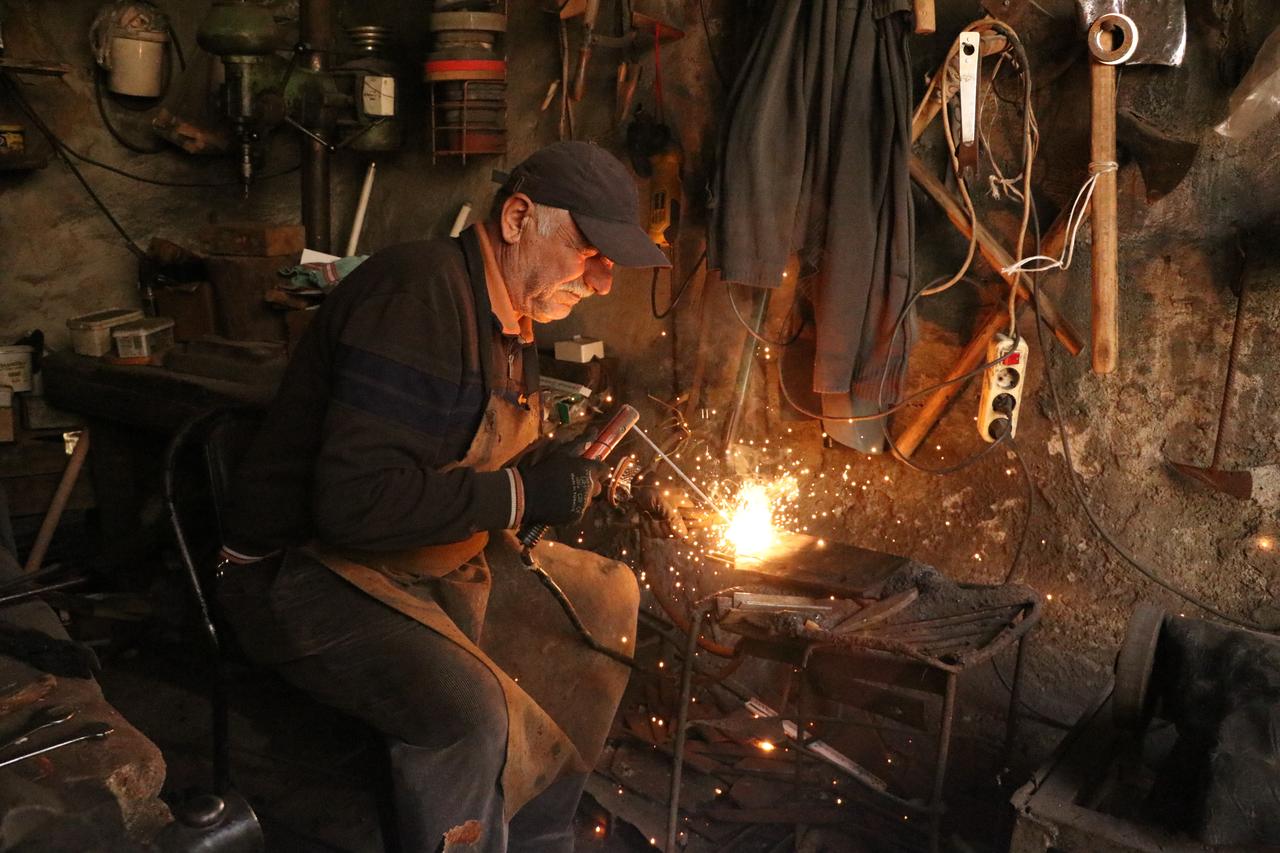 Blacksmith Remzi uses a welding tool to shape metal as sparks fly inside his workshop in Türkiye, Oct. 23, 2026. (AA Photo)