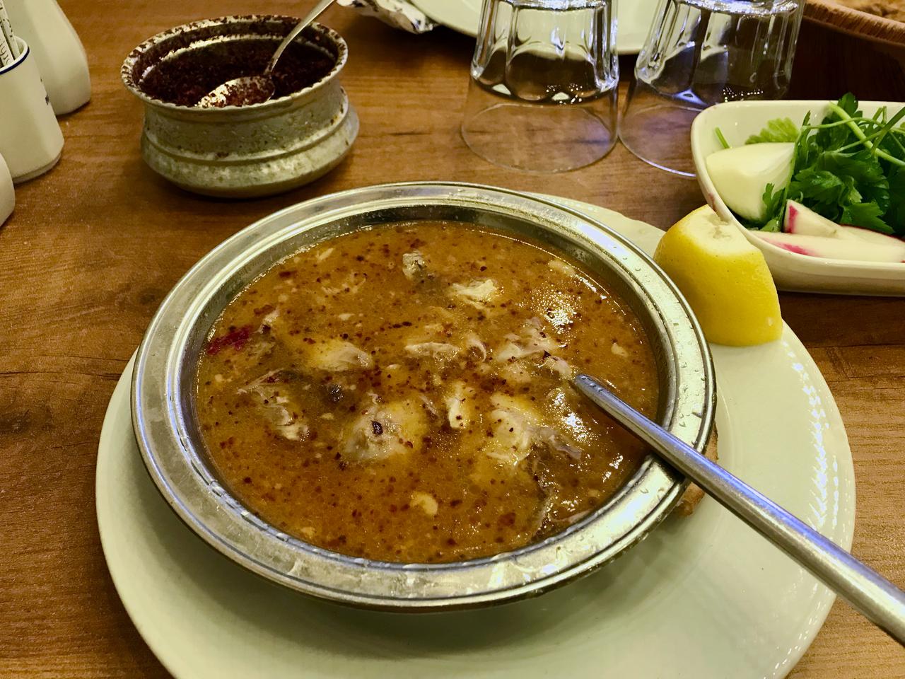 A traditional bowl of meat soup served with lemon, fresh herbs and seasonings at a restaurant. (Adobe Stock Photo)