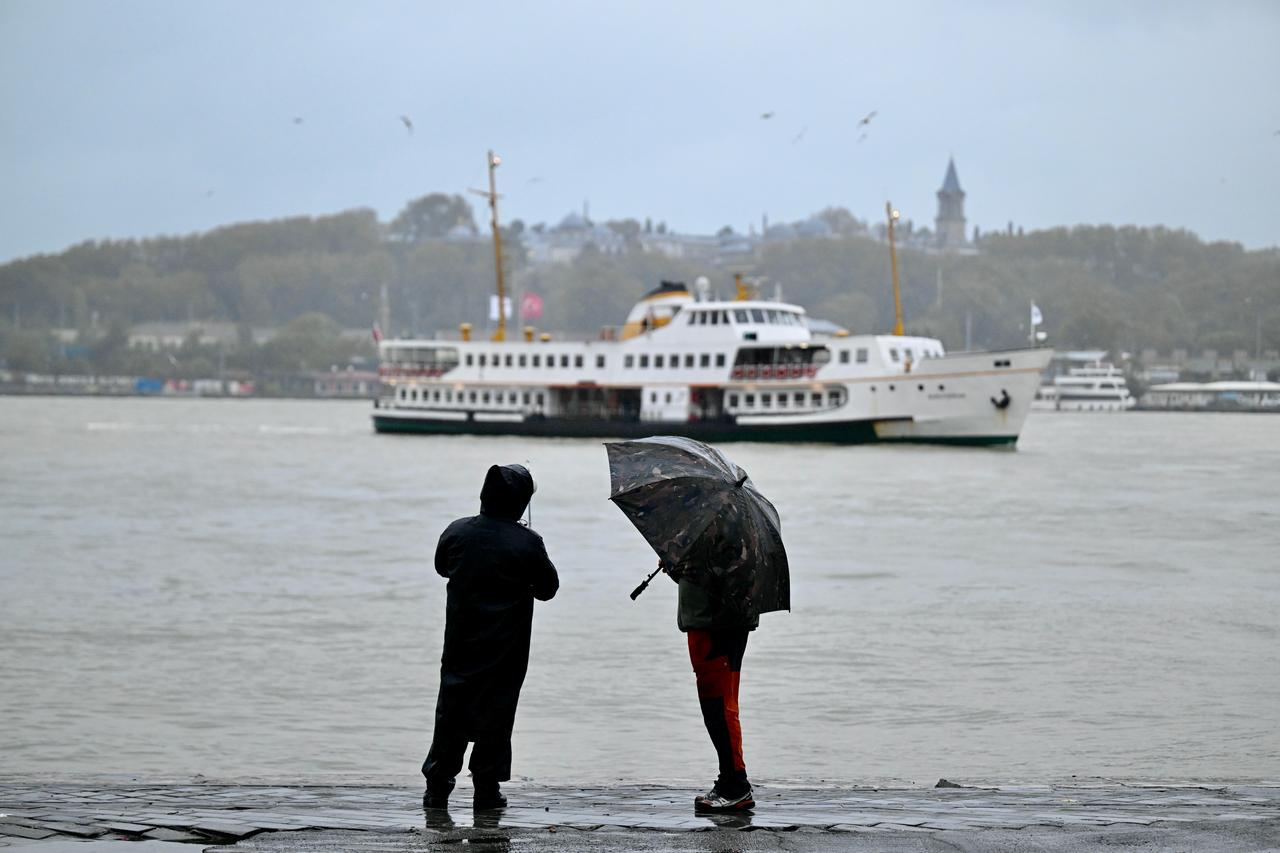Two people stand with umbrellas along the waterfront as a passenger ferry crosses the Bosphorus in Istanbul, Türkiye, Oct. 15, 2026. (AA Photo)