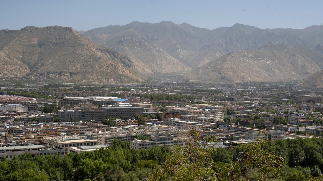 A panoramic view of Lhasa, Tibet, China, showing densely packed urban buildings surrounded by trees and the Himalayan mountain range. (Adobe Stock Photo)