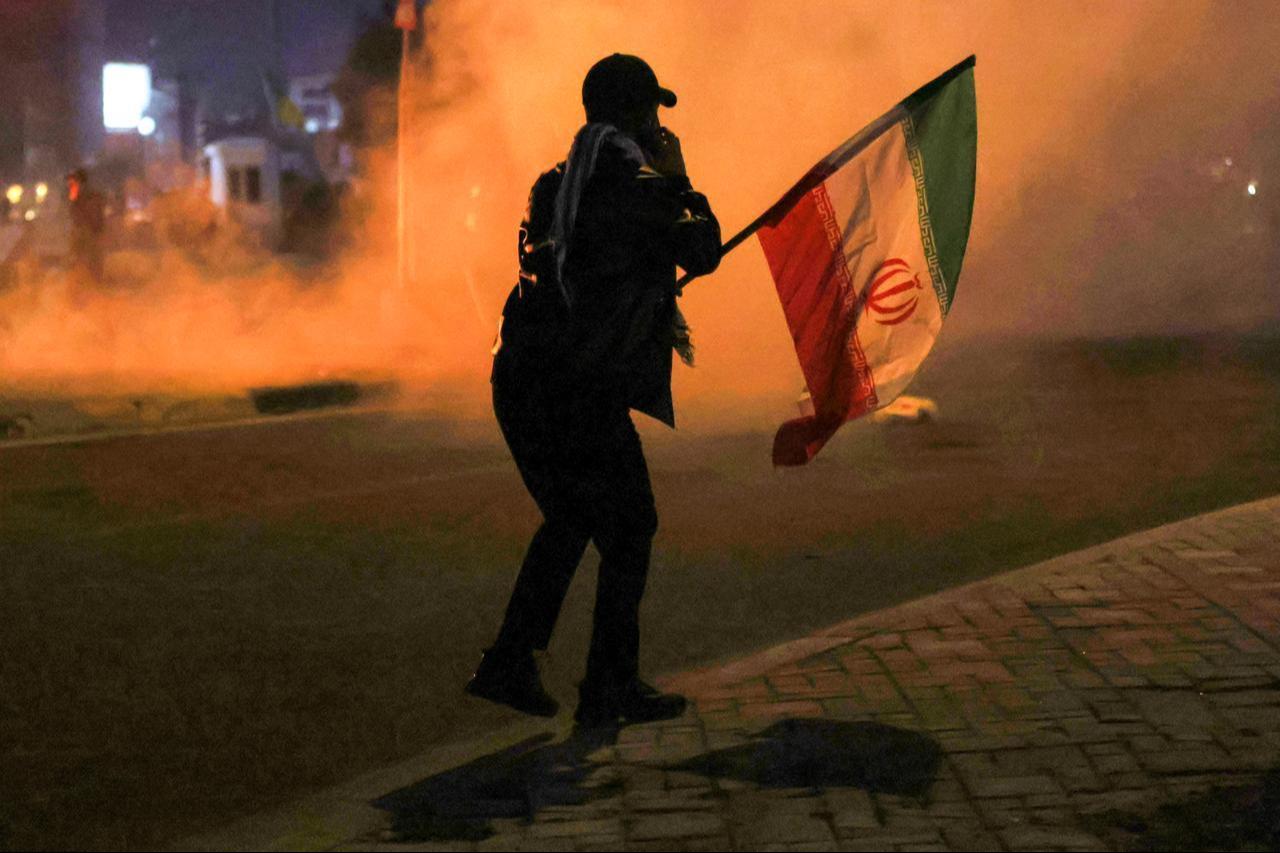A person waving an Iranian flag walks near tear gas fumes as protesters clash with Iraqi security forces as they try to approach a bridge leading to the Green Zone where the US embassy is located in Baghdad on March 1, 2026, the morning after the US and Israel targeted Iran. (AFP Photo)