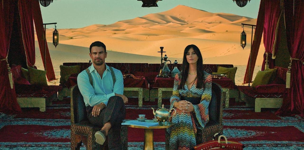 Theo James and Kaya Scodelario sit inside a decorated desert tent with sand dunes in the background. (Photo via social media)