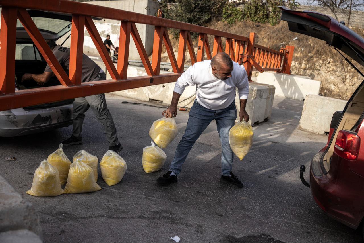 People pass packages under a closed checkpoint gate at one of the entrances to the Israeli-occupied West Bank city of Hebron on October 24, 2026. (AFP Photo)