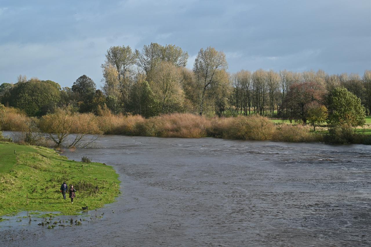 Two people walk along the banks of a swollen river following heavy rainfall in Britain, Oct. 25, 2026. (AFP Photo)