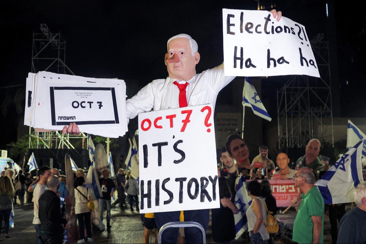 A protester wearing a mask depicting Israeli Prime Minister Benjamin Netanyahu with an elongated nose, evoking the literary character Pinocchio, poses with a placard during an anti-government demonstration at the Hostages Square in Tel Aviv, Oct. 24, 2026, ahead of Israel's legislative election. (Photo by Jack GUEZ / AFP)
